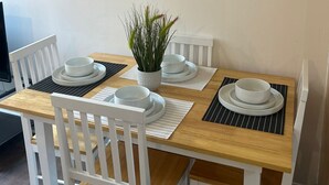 Ein Esstisch mit weißen Stühlen, einem Blumentopf und abstrakter Wandkunst.