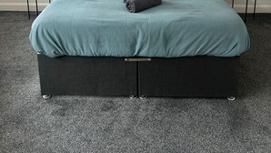 Ein Schlafzimmer mit einem Bett, zwei Nachttischen, zwei abstrakten Gemälden und zwei Vasen mit Pampasgras.
