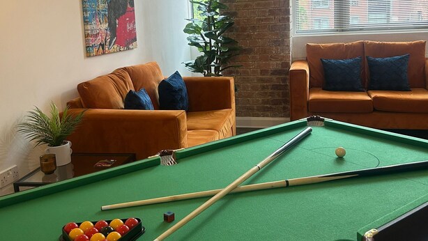 Ein Billardtisch in einem Wohnzimmer mit zwei Sofas und einem großen Fenster.