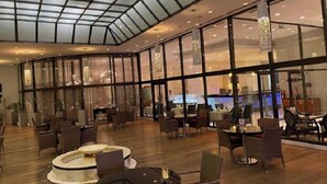 A spacious lobby with a high ceiling and large windows, featuring a variety of seating arrangements and a central decorative element. - Hotel El Aurassi (Algiers)