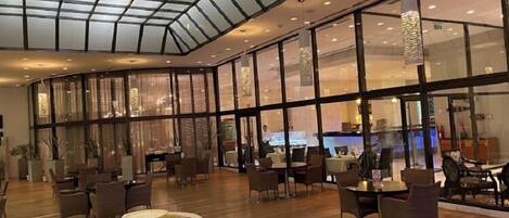 A spacious lobby with a high ceiling and large windows, featuring a variety of seating arrangements and a central decorative element.