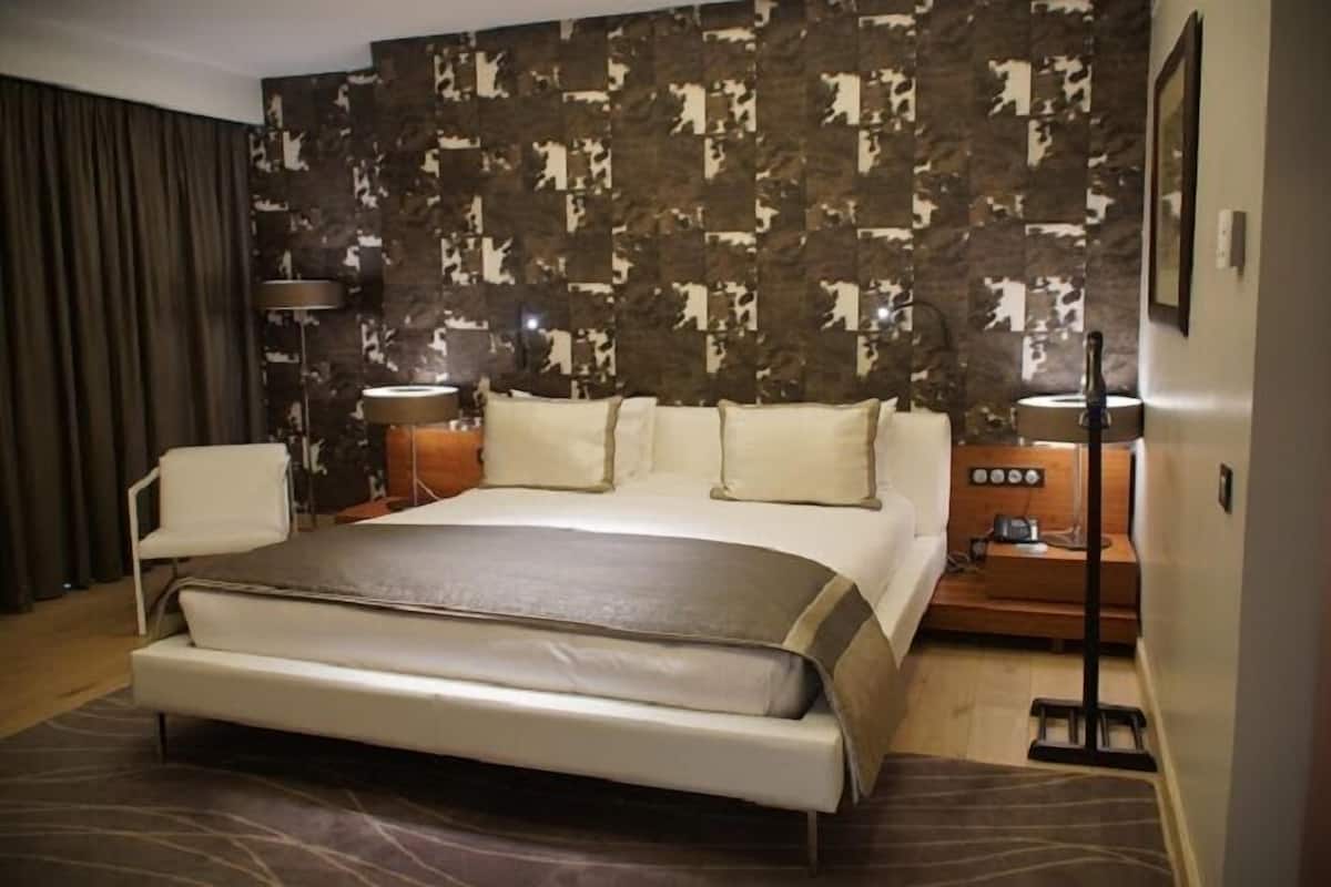 A modern hotel room with a large bed, a bedside table, a lamp, and a wall with a camouflage pattern.