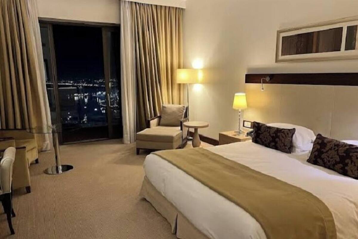 A hotel room with a large bed, a chair, a small table, and a view of the city at night.