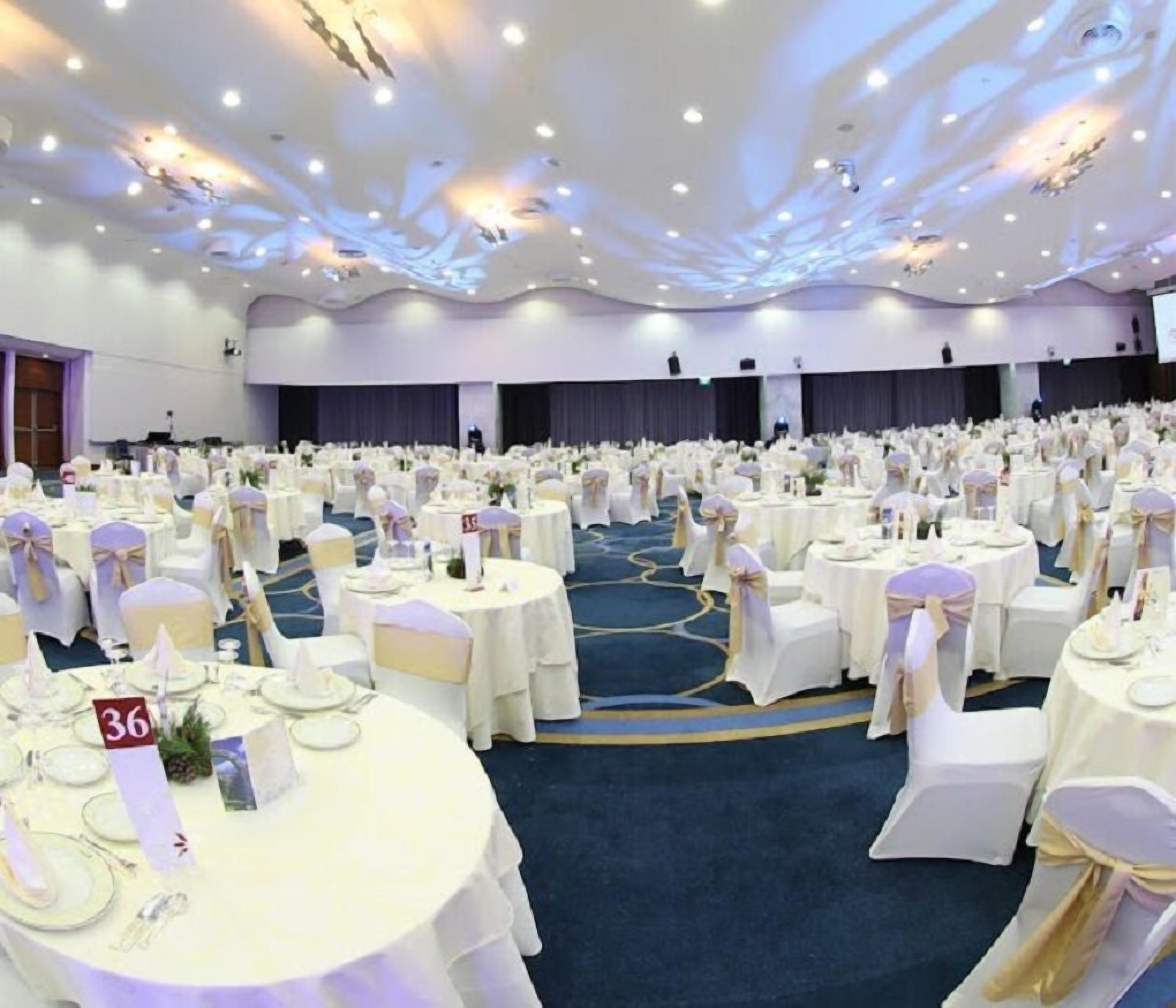 A large banquet hall with round tables set for events, featuring a blue carpet and white tablecloths.