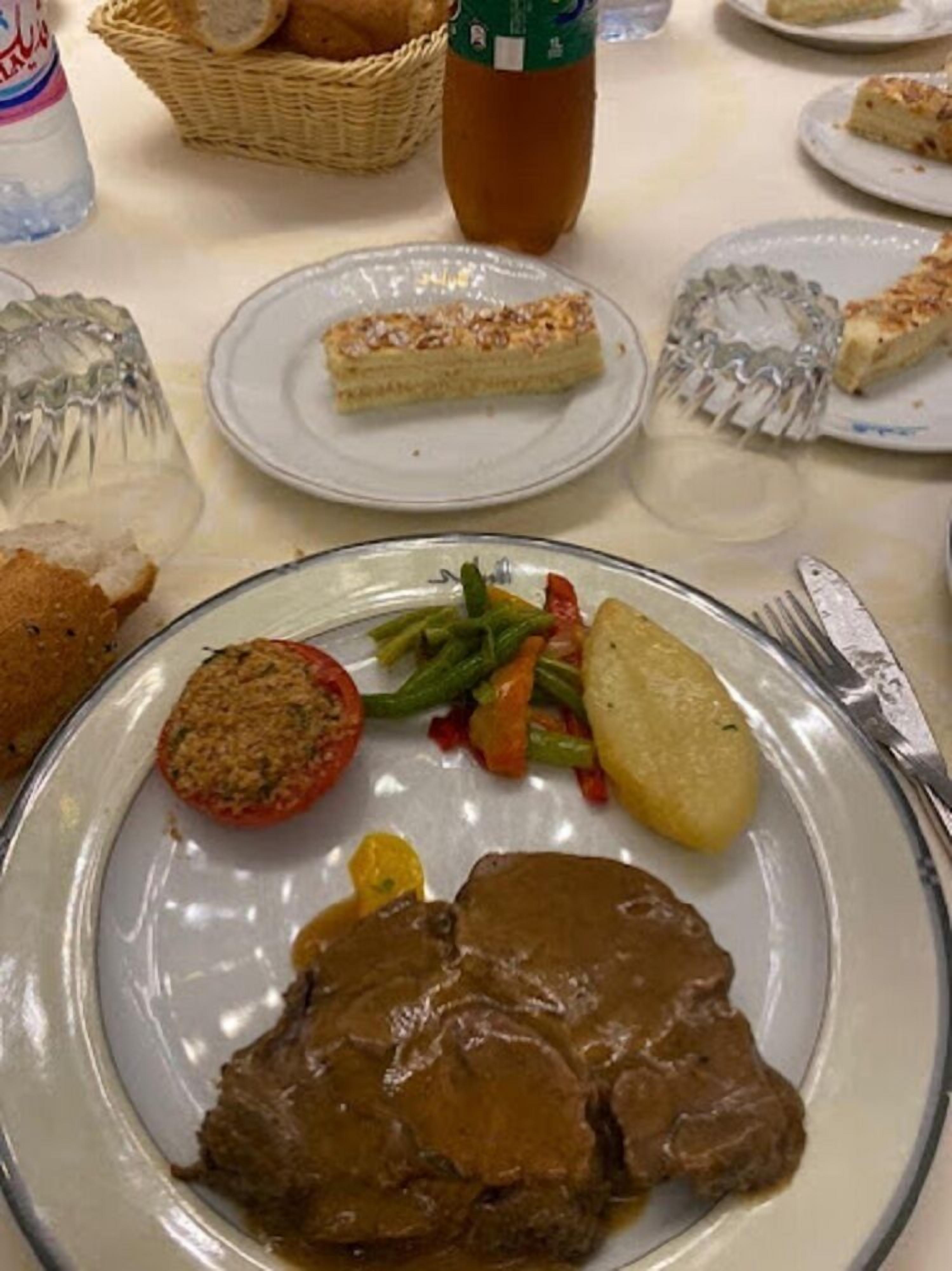 A dining table with various dishes including a plate of meat with gravy, vegetables, and a slice of cake.