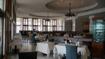 Un restaurante espacioso con techos altos, grandes ventanales y una zona de bar central. Las mesas están dispuestas con manteles blancos y sillas.