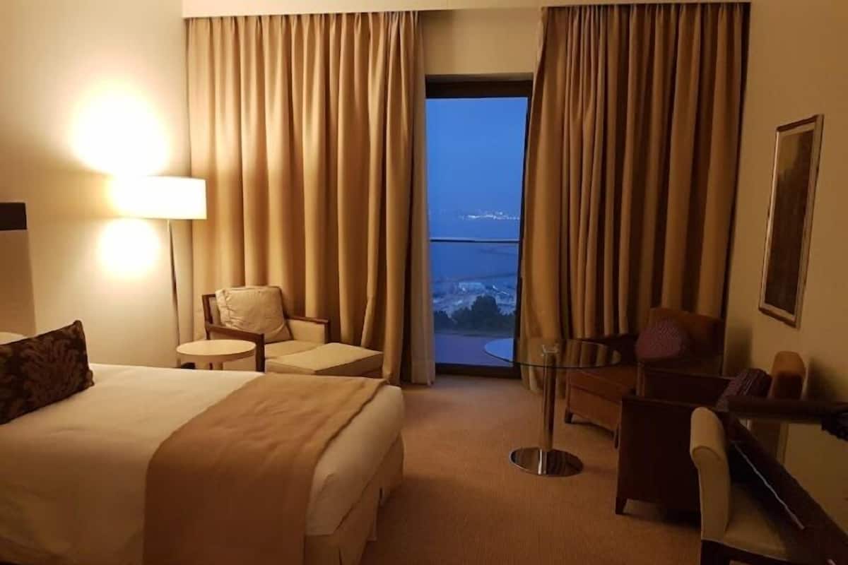 A hotel room with a bed, two armchairs, a small table, and a desk. There is a large window with curtains, and a view of a snowy landscape.