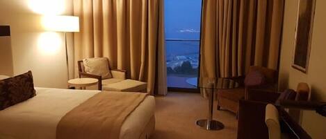 A hotel room with a bed, two armchairs, a small table, and a desk. There is a large window with curtains, and a view of a snowy landscape.
