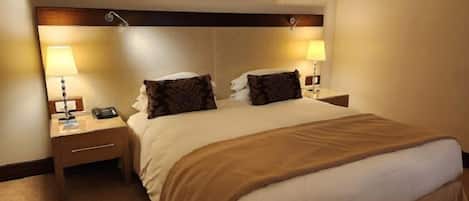 Habitación de hotel con una cama grande, dos mesitas de noche, lámparas y un cabecero con un panel decorativo.