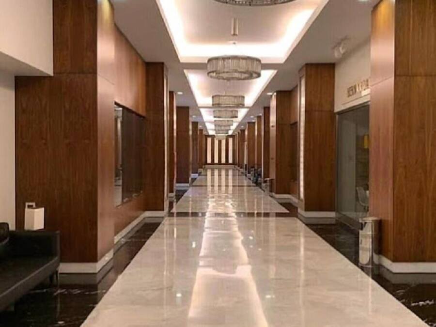 A long, polished hallway with wooden paneling and a reflective floor, leading to a reception area with a chandelier.