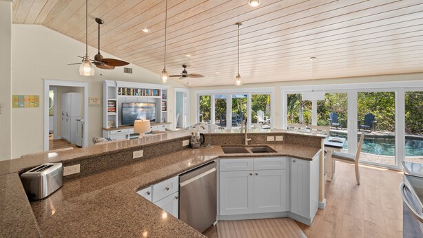 A modern kitchen with granite countertops, white cabinets, and a large island. There is a dining area with a view of the pool. - Paradise Pointe by Beach Boutique Rentals (Anna Maria)