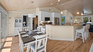A modern kitchen with white cabinets, a central island, and a dining area with a table and chairs. - Paradise Pointe by Beach Boutique Rentals (Anna Maria)