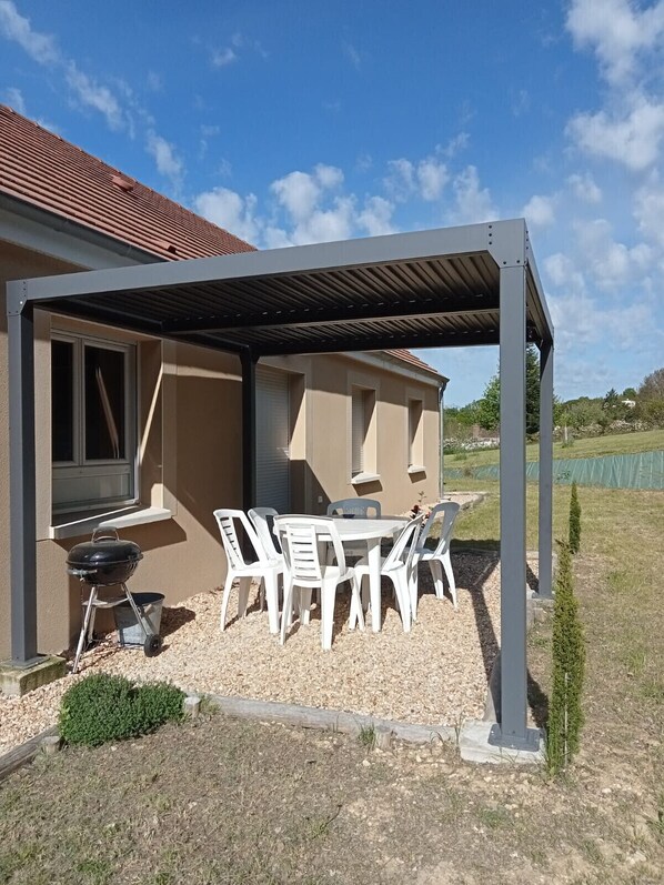 A covered patio area with a grill, white plastic chairs, and a table.