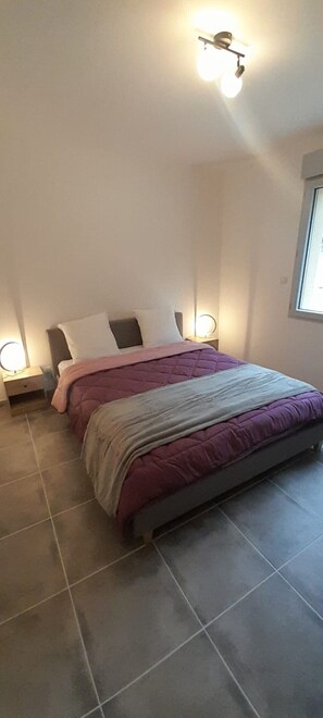 A bedroom with a bed, two bedside tables, a nightstand, a ceiling fan, and a window.