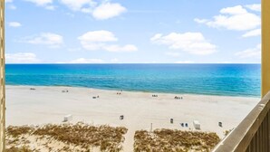 Blick auf einen Strand vom Balkon aus, mit blauem Himmel, Sandstrand und Meer.