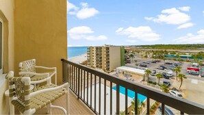 Ein Balkon mit Korbstühlen, Blick auf einen Strand, einen Parkplatz und ein Gebäude mit Schwimmbad.