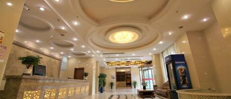 A hotel lobby with a reception desk, a large chandelier, and a tiled floor.