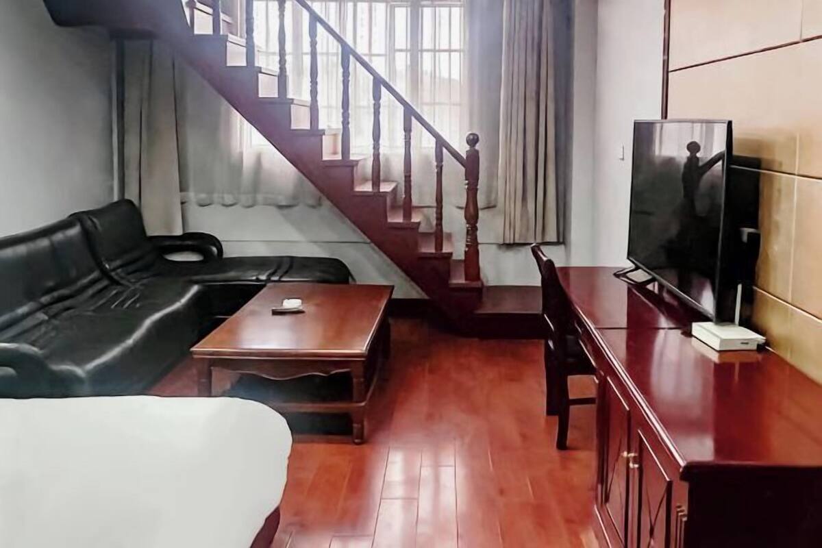 A living room with a wooden staircase, a black leather sofa, a wooden coffee table, a TV on a wooden cabinet, and a white chair.