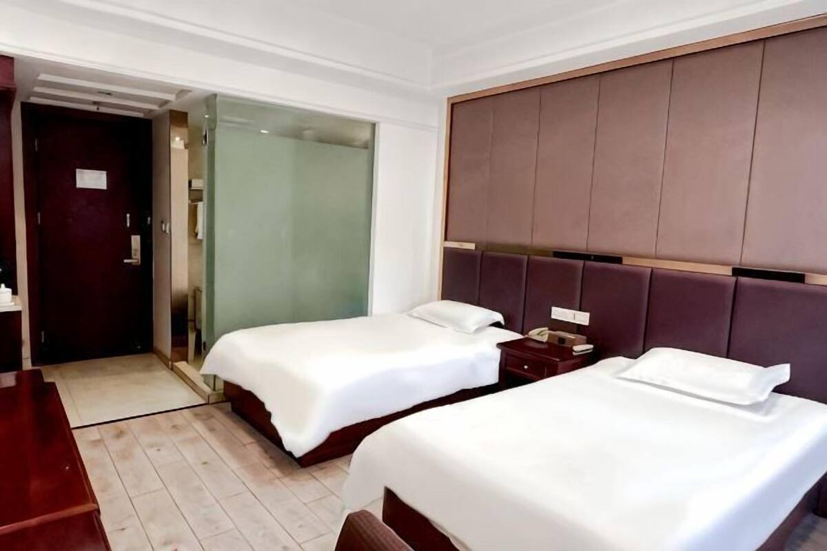 A hotel room with two beds, a desk, and a glass shower enclosure.