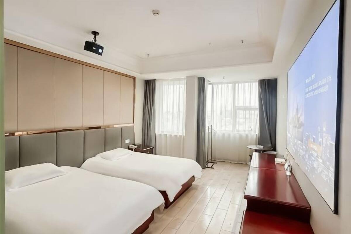 A hotel room with two beds, a TV, a desk, and a large window.