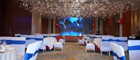 A banquet hall with round tables, white chairs, and a large screen at the front.