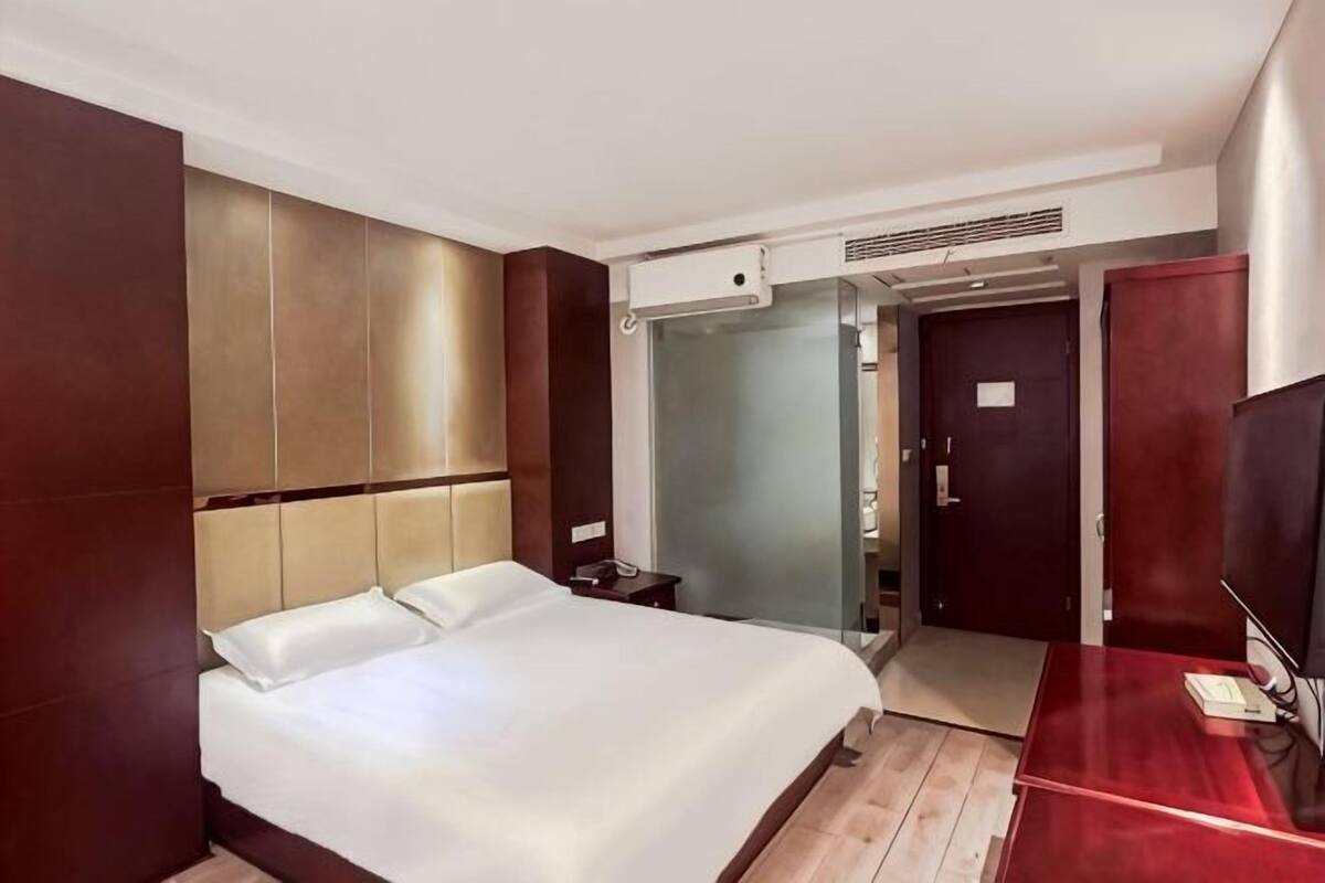 A hotel room with a large bed, a desk with a chair, a mirror, and a wardrobe.