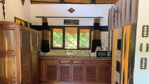 A compact kitchen with wooden cabinets, a sink, a window with curtains, and a microwave on the counter. - Sabi Star Accommodation (Mutare)