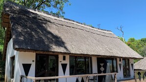A traditional thatched-roof building with a white exterior, large windows, and a wooden railing in front. - Sabi Star Accommodation (Mutare)
