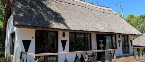 A traditional thatched-roof building with a white exterior, large windows, and a wooden railing in front.