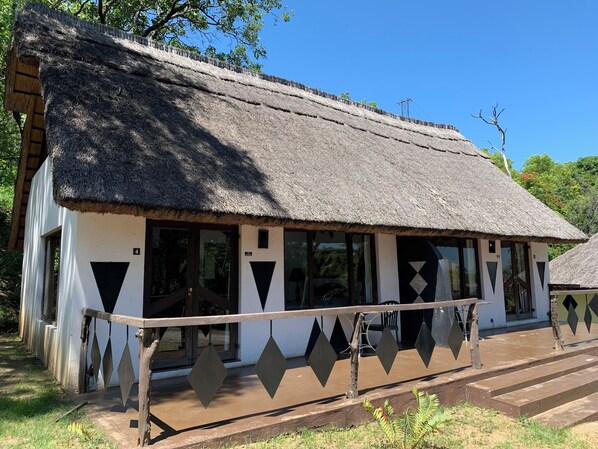 A traditional thatched-roof building with a white exterior, large windows, and a wooden railing in front. - Sabi Star Accommodation (Mutare)