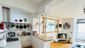 A modern kitchen with white cabinets, a wooden countertop, and a gas stove. There is a dining area with a glass table and a sofa. - Luxury Seacliff Apartment overlooking Ventnor Beach, Sleeps 4 , Ferry Discounts (Ventnor)