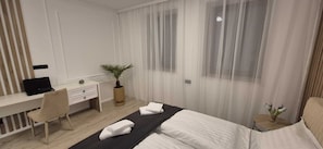 A modern hotel room with a bed, a desk, a laptop, a plant, and a small table with a vase.