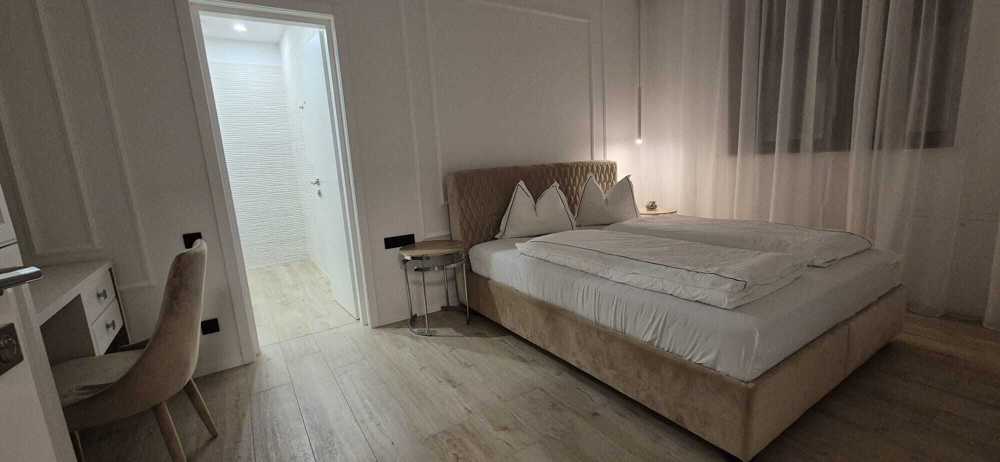 Een slaapkamer met een bed, nachtkastjes, een stoel en een deur die naar een andere kamer leidt.