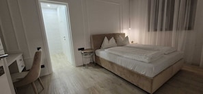 A bedroom with a bed, bedside tables, a chair, and a door leading to another room.