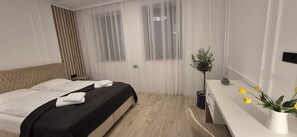 Una habitación de hotel moderna con una cama, una mesita de noche, una planta en maceta y una ventana con cortinas traslúcidas.