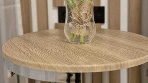 A round table with a woven top and metal legs, holding a glass vase with a burlap base and a single tulip. - Anita's mansion (Gattendorf)