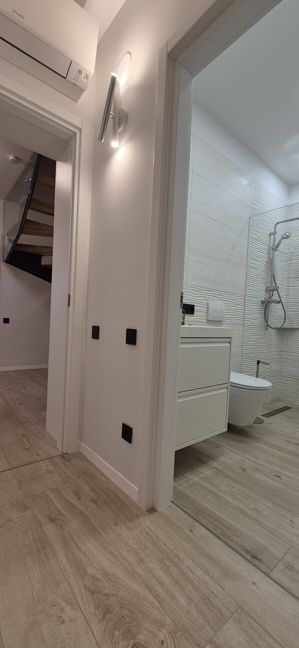 Une salle de bain moderne avec une douche à parois de verre, un lavabo blanc et un escalier en bois.