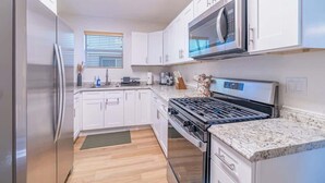 A modern kitchen with white cabinets, a stainless steel refrigerator, a built-in microwave, and a gas stove. - Charming Family 2BR Midtown Reno - Pets Welcome (Reno)