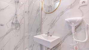 Un baño con ducha de mármol, lavamanos y secador de pelo.