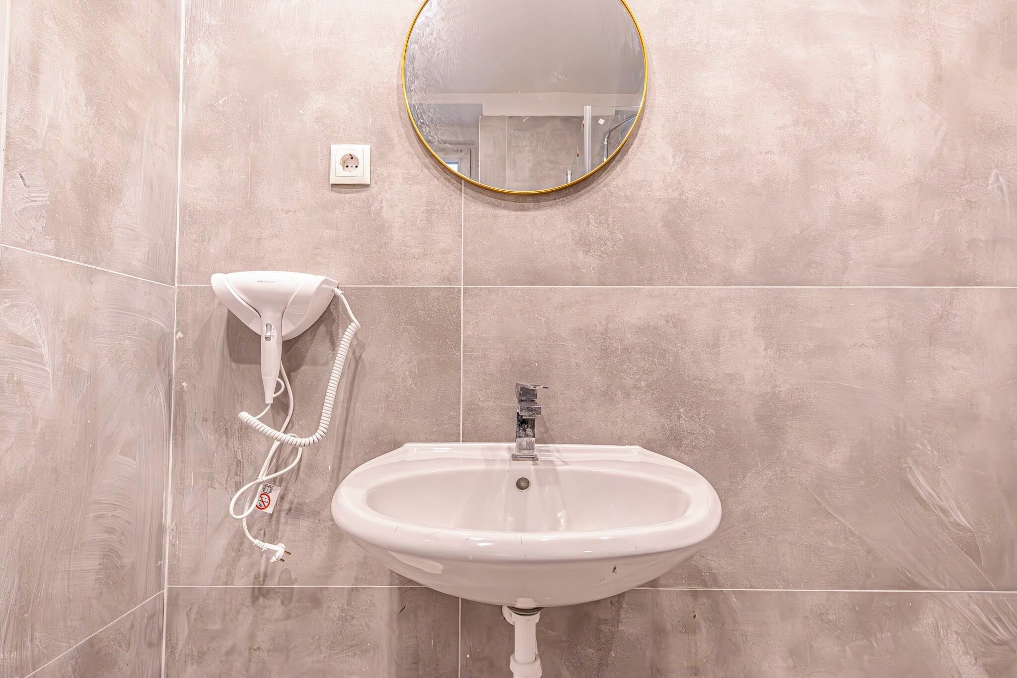 A bathroom with a white sink, a round mirror, and a white telephone.