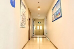 Un couloir d’hôtel avec un sol carrelé, une porte au fond et des affiches d’information accrochées aux murs.