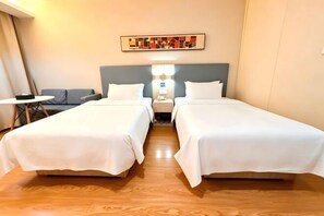 Une chambre d’hôtel avec deux lits, une petite table, une chaise, une table de chevet et une lampe.