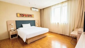 Una habitación de hotel con cama, mesitas de noche, unidad de aire acondicionado, ventana con cortinas y una obra de arte colgada en la pared.