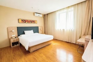 A hotel room with a bed, bedside tables, an air conditioning unit, a window with curtains, and a wall-mounted artwork.