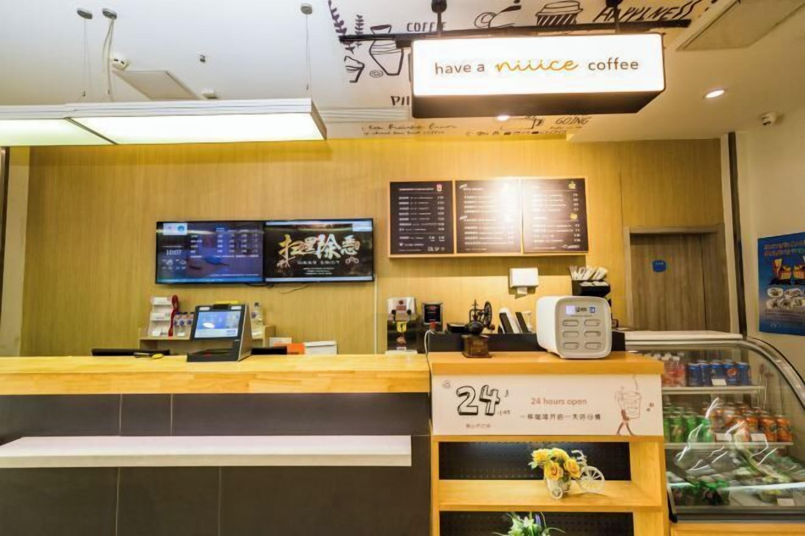 A coffee shop interior with a wooden counter, digital menu boards, and a 24-hour sign.