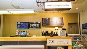 Un interior de cafetería con un mostrador de madera, pantallas digitales con el menú y un letrero de '24 horas'.
