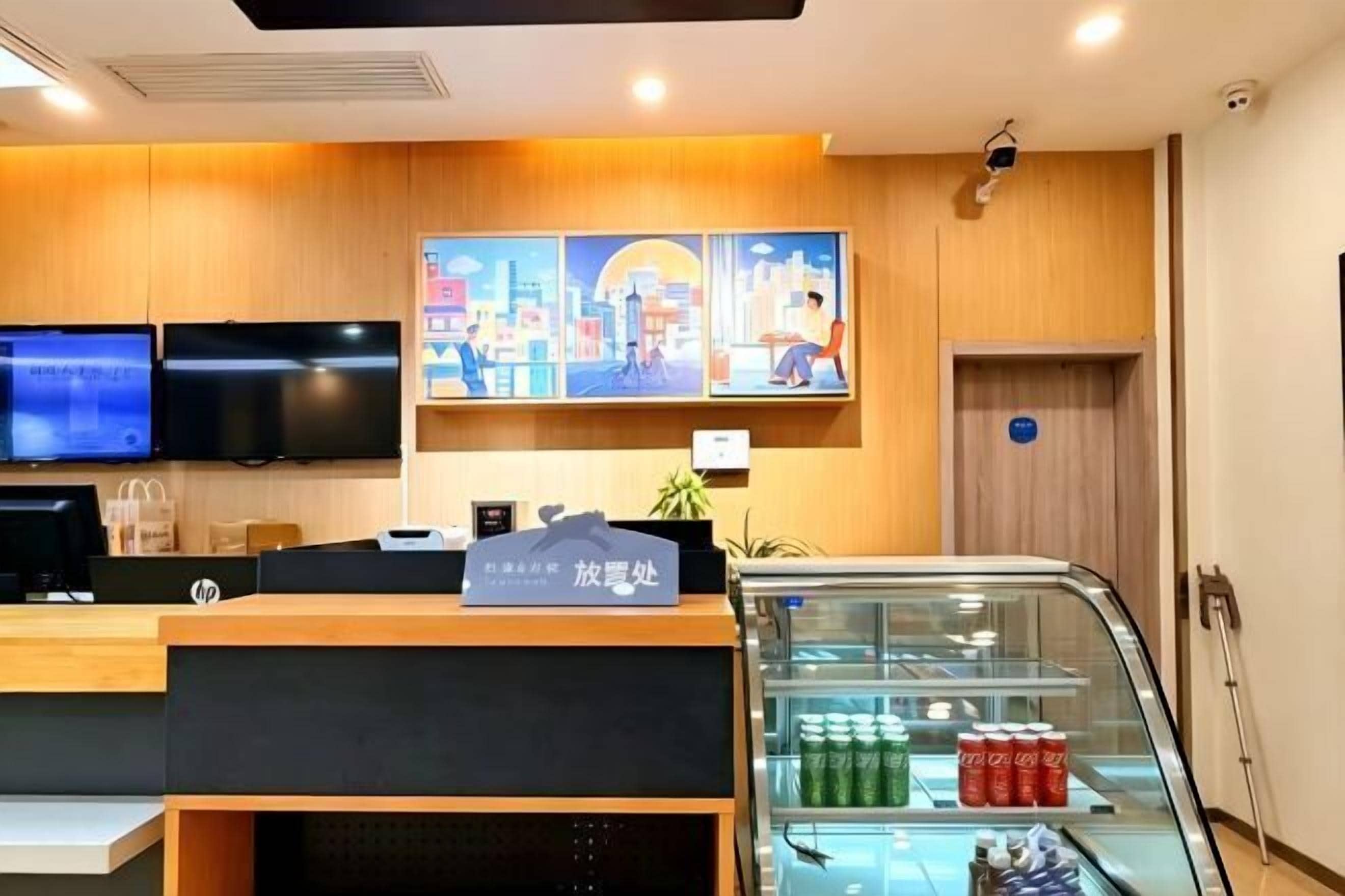 A hotel reception area with a wooden interior, a glass display case with beverages, and two flat-screen TVs mounted on the wall.