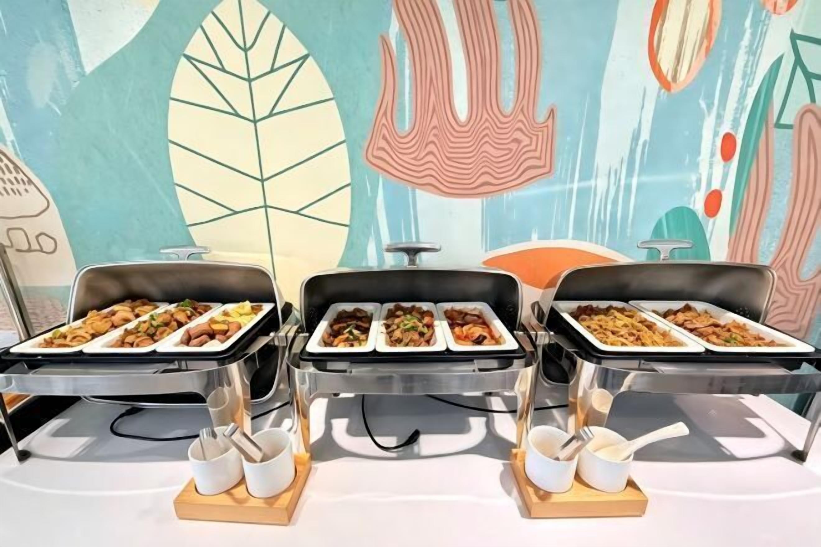 Buffet stations with trays of food, serving utensils, and a colorful abstract wall mural in the background.
