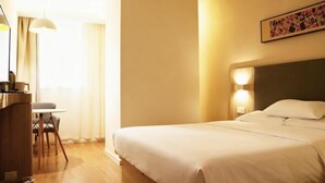 Una habitación de hotel con cama, mesita de noche, lámpara y escritorio con silla.