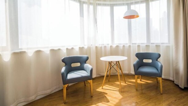Una habitación con dos sillas azules, una mesita blanca y un ventanal con cortinas de encaje.